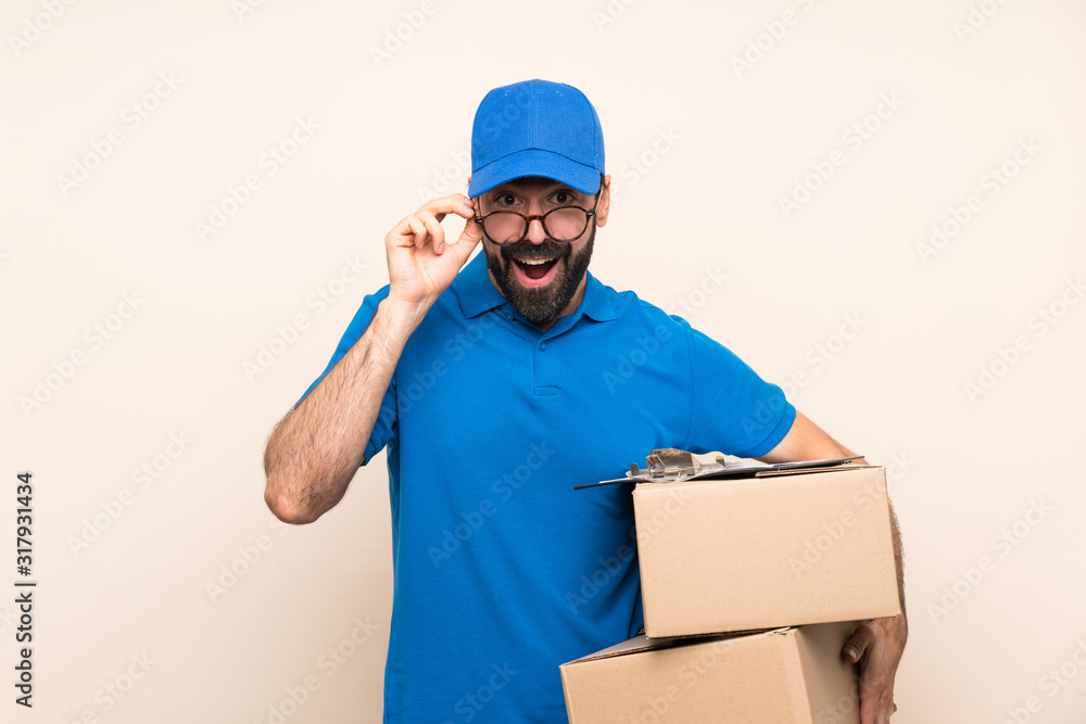 Delivery man with beard over isolated background with glasses and surprised Delivery man with beard over isolated background with glasses and surprised