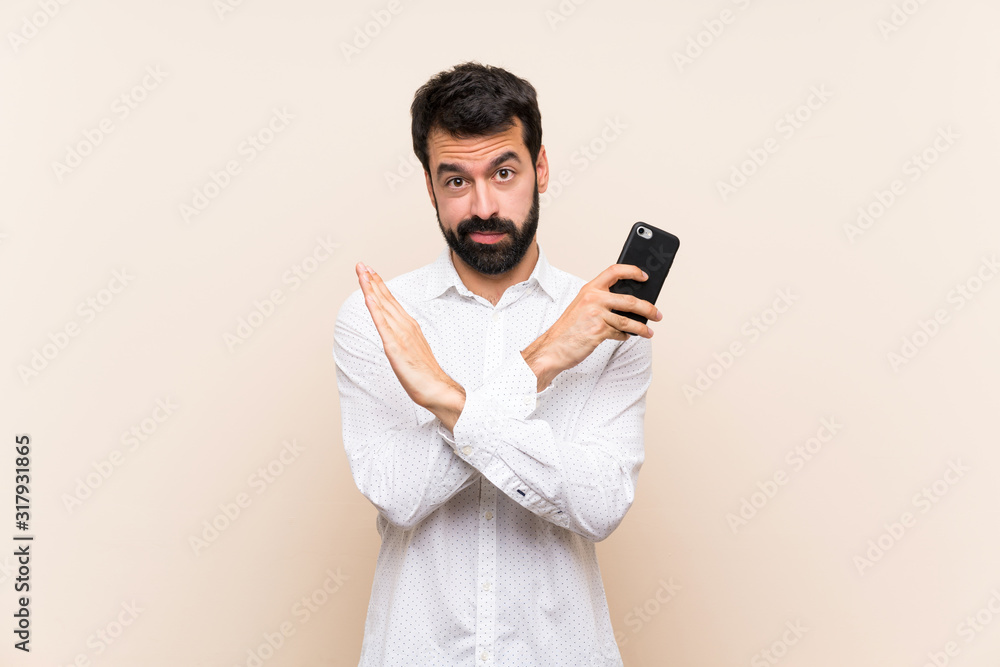 Young man with beard holding a mobile making NO gesture Young man with beard holding a mobile making NO gesture