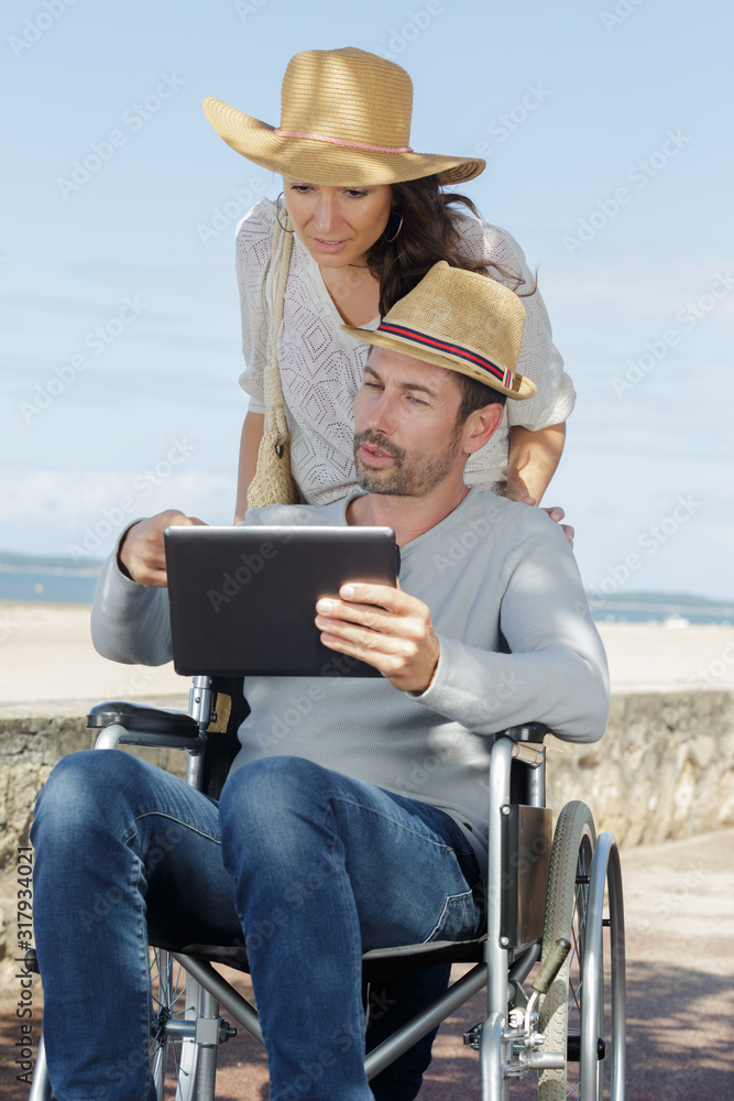 couple by beach looking at tablet man in wheelchair