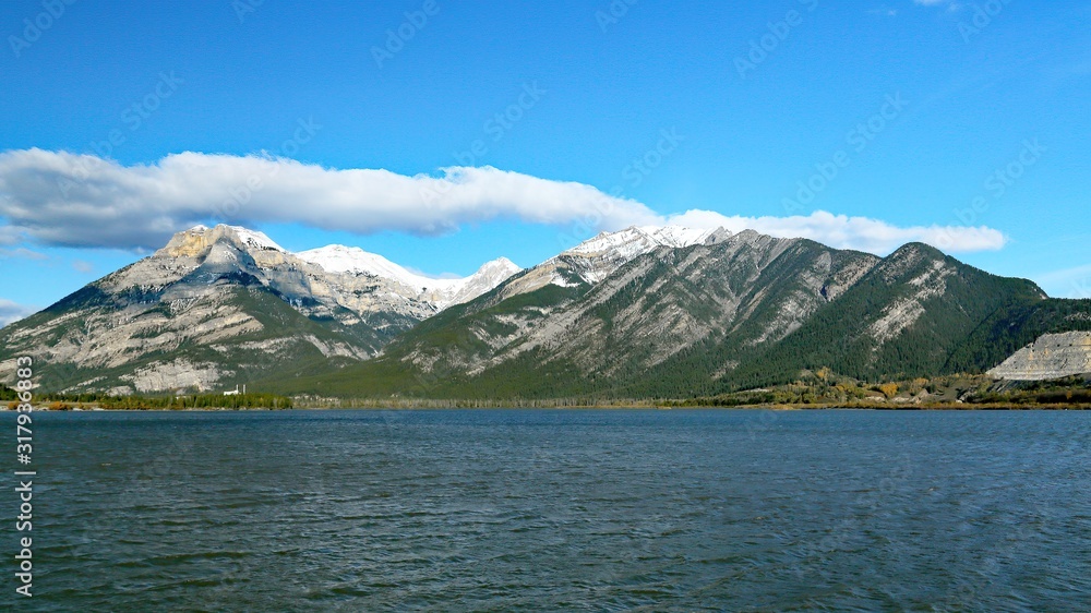 Blue sky with clouds and blue lake with mountains in the background