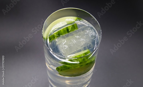 Top view on isolated glass with sparkling tonic water, cucumber slices, gin and ice cubes, white gray background