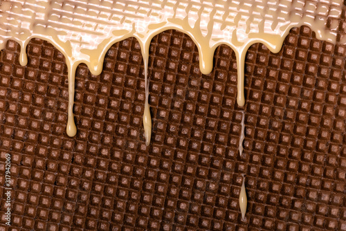 Waffle covered with condensed milk close-up. White hot chocolate spreads on the wafer. Tasty food