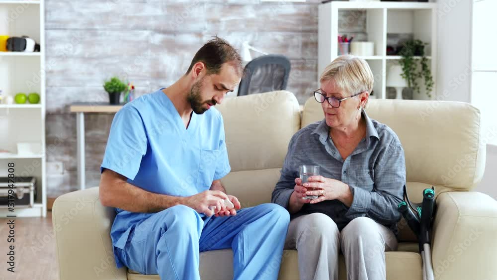Male nurse sitting on couch with senior woman giving her medical treatment in nursing home Male nurse sitting on couch with senior woman giving her medical treatment in nursing home