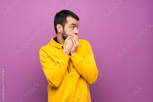 Handsome man with yellow sweatshirt covering mouth and looking to the side © luismolinero