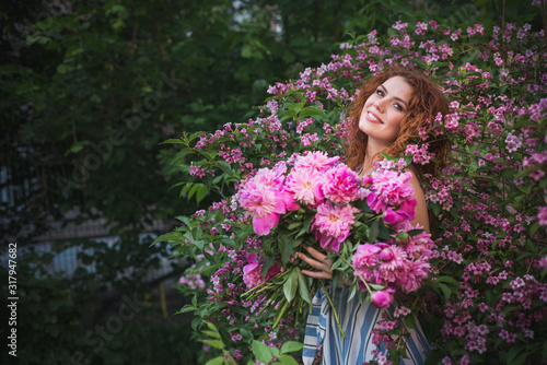 Close up romantic portrait of beautiful young woman in blossom spring garden with bouquet of peonies