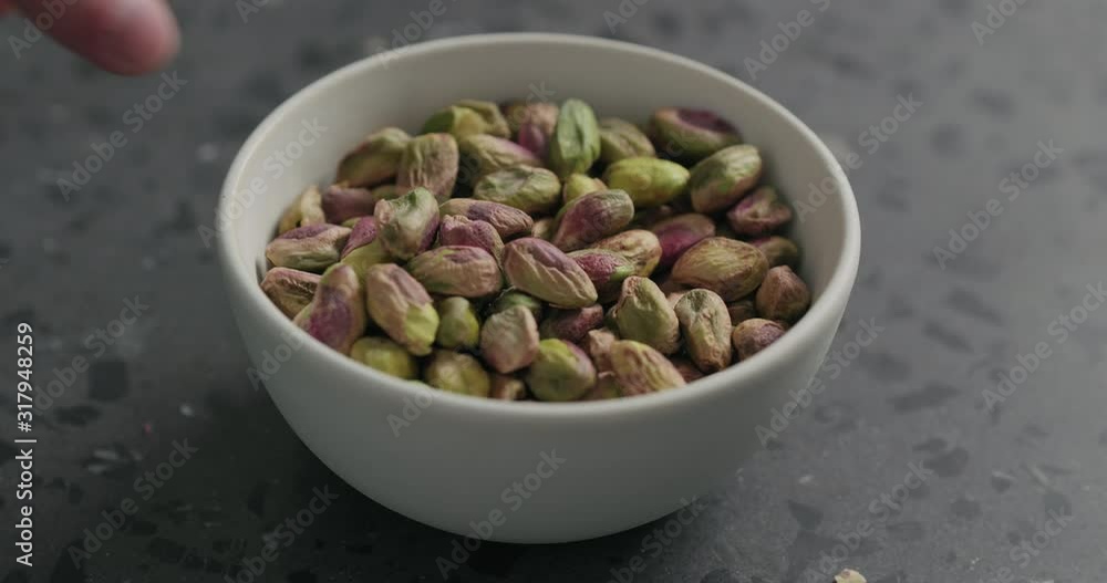 Slow motion man hand takes pistachio kernels from white bowl on terrazzo surface Slow motion man hand takes pistachio kernels from white bowl on terrazzo surface
