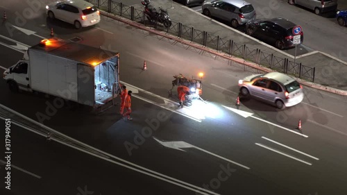 Road workers in protective uniform repairing asphalt at night in Rome. Men painting new white road marking lines on surface, renovation of road signs, teamworkers repairing road with special machinery photo