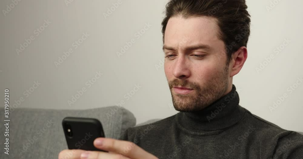 Young men relaxing on couch using smart phone in house. Young guy write sms , a list of cases. Сoncentrated person.Indoors Young men relaxing on couch using smart phone in house. Young guy write sms , a list of cases. Сoncentrated person.Indoors