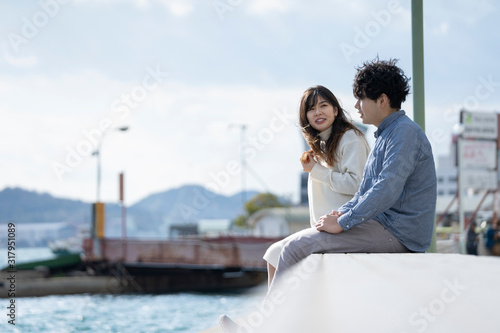 堤防に腰掛け楽しそうに会話をする若いカプル © west_photo