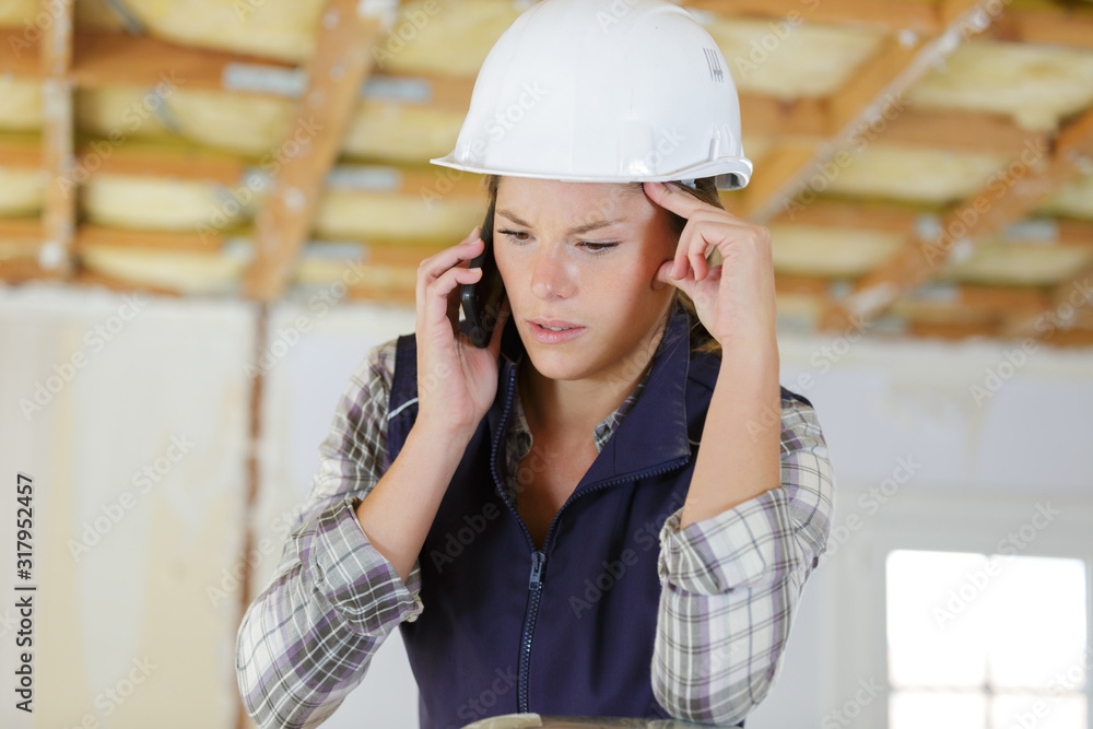 worried female builder using cellular telephone