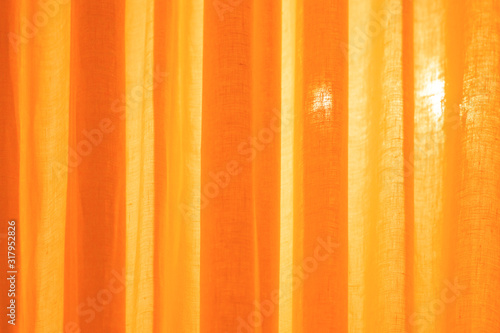 Translucent textile monochrome orange curtains and a beam of light radiating through them