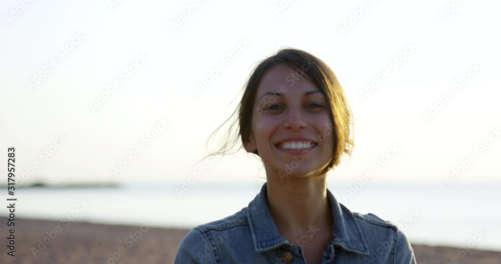 Young attractive woman on beach smiles towards camera - medium shot handheld Young attractive woman on beach smiles towards camera - medium shot handheld