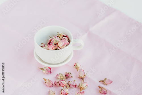 Selective focus on dried roses in a white cup at pink pastel background. Copy space.