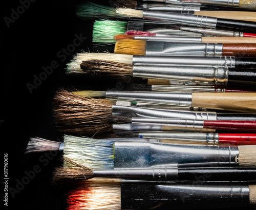 different used paint brushes on a black background