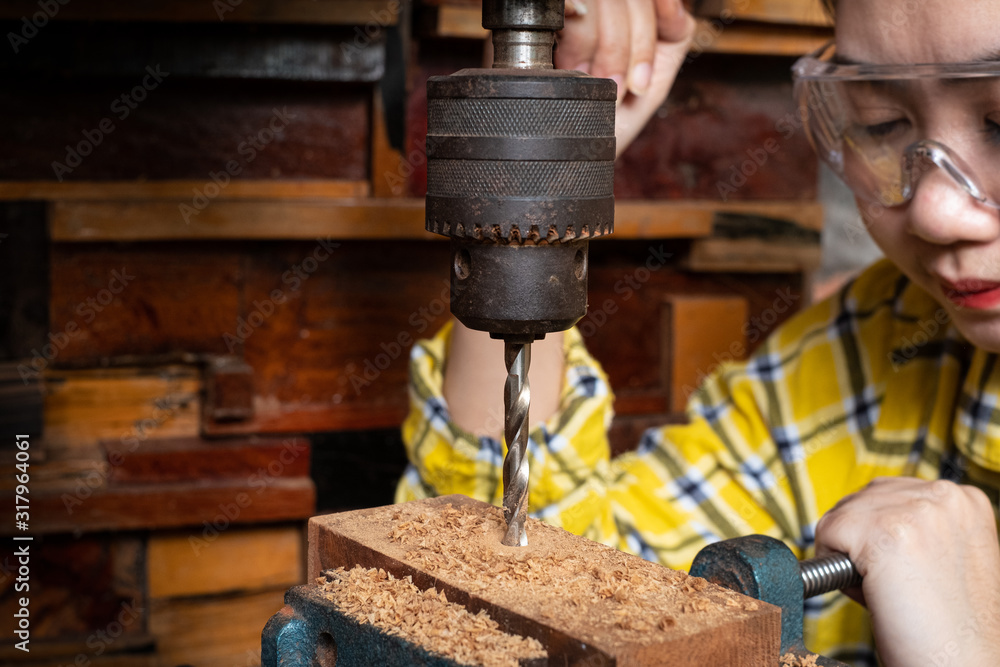 Women standing is craft working drill wood at a workbench with Drill Press power tools at carpenter machine in the workshop