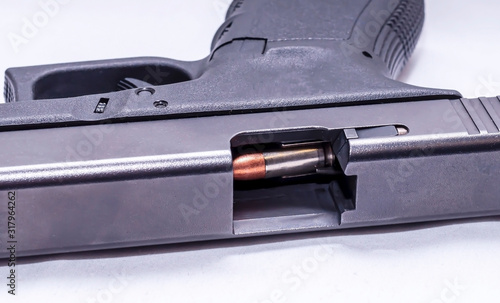 A black 9mm semi automatic pistol on it's side with an opened slide showing a 9mm bullet through the ejection port on a white background 