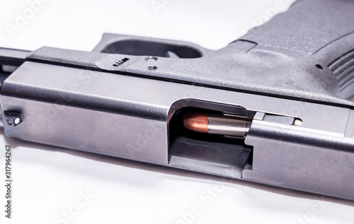 A black 9mm semi automatic pistol on it's side with an opened slide showing a 9mm bullet through the ejection port on a white background 