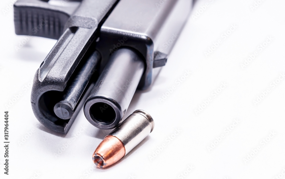 A black 9mm semi automatic with it's slide opened showing the barrel with a single 9mm hollow point bullet next to it on a white background A black 9mm semi automatic with it's slide opened showing the barrel with a single 9mm hollow point bullet next to it on a white background