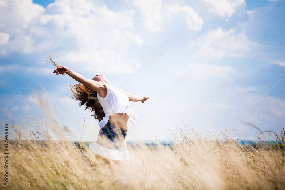 Young woman in casual clothing standing in rye field and enjoying sunshine on summer day with blue sky at background Young woman in casual clothing standing in rye field and enjoying sunshine on summer day with blue sky at background