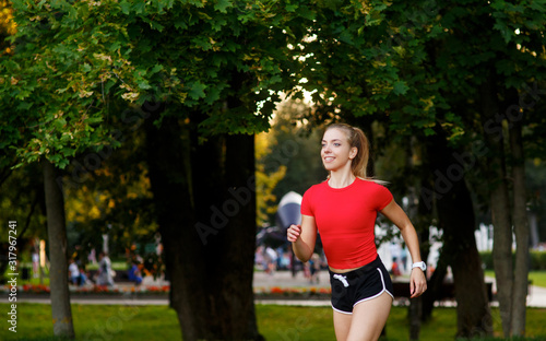 A young girl goes in for sports outdoors. woman in shorts and red t-shirt runs in nature