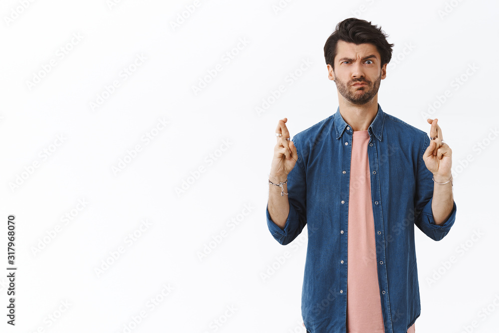 Intense, skeptical handsome man cross fingers good luck but have doubts if dream come true, frowning and smirk hesitant, praying with disbelief in miracle, weighing possibility of achievement happen Intense, skeptical handsome man cross fingers good luck but have doubts if dream come true, frowning and smirk hesitant, praying with disbelief in miracle, weighing possibility of achievement happen