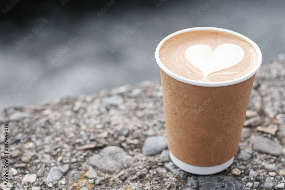 Hot coffee paper cup against river background, heart shape latte coffee ...