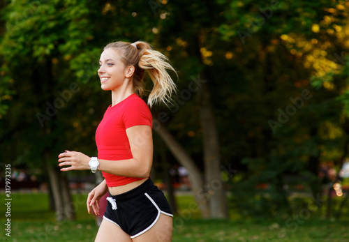 A young girl goes in for sports outdoors. woman in shorts and red t-shirt runs in nature