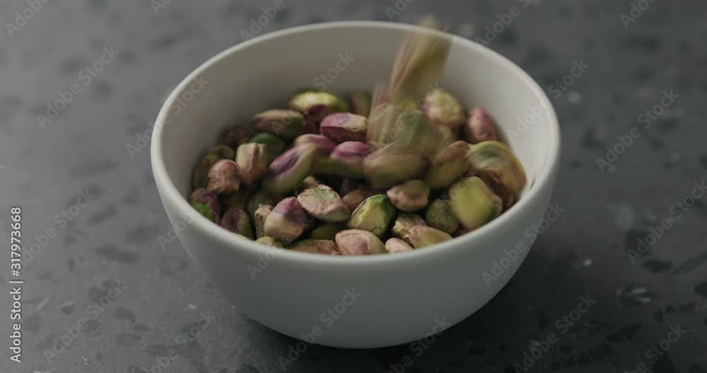 Slow motion peeled pistachios falls into white bowl on terrazzo surface Slow motion peeled pistachios falls into white bowl on terrazzo surface