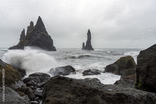 Waves crashing in on shore on Reynisfjara near the city of Vik in Iceland. Basalt sculpture columns raises up from the sea in the background. Rocks infront. Traveling and nature concept.