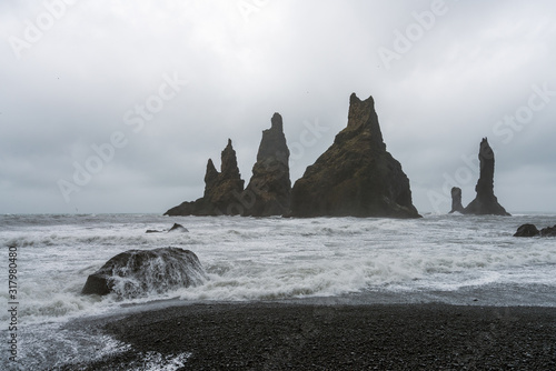 Waves crashing in on shore on Reynisfjara beach and black volcanic sand in Iceland. Basalt sculpture columns raises up from the sea in the background. Traveling and nature concept.