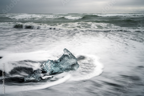 Crystal clear and blue ice chunks washes up on the black lava sand by the waves on diamond beach in Jokulsarlon glacier lagoon. Long exposure shot. © Jon Anders Wiken