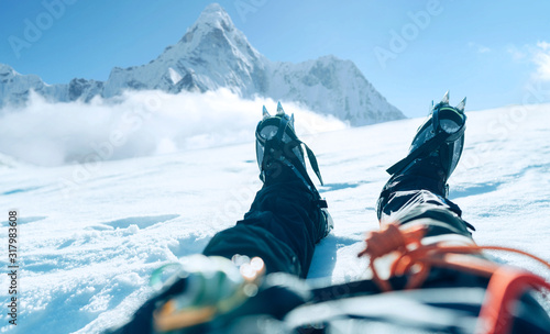 POV shoot of a high altitude mountain climber's lags in crampons. He lying and resting on snow ice field with Ama Dablam (6812m) summit covered with clouds background.Extremal people vacations concept