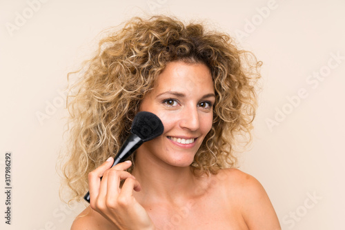 Young blonde woman with curly hair with makeup brush