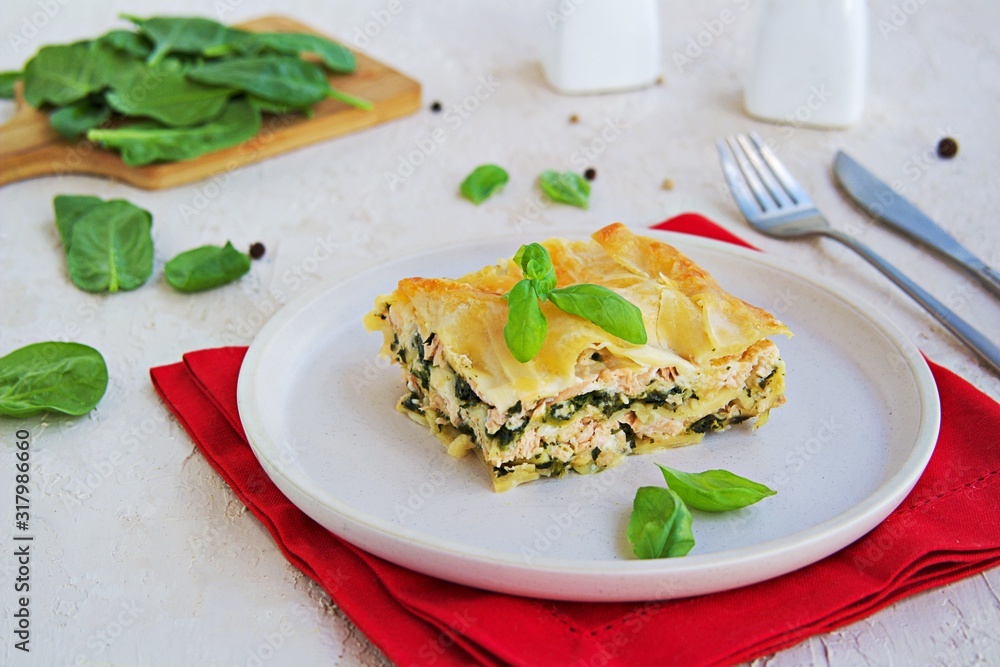 Lasagna with salmon and spinach on a clay plate on a light concrete background. Italian food. Pasta Recipes Lasagna with salmon and spinach on a clay plate on a light concrete background. Italian food. Pasta Recipes