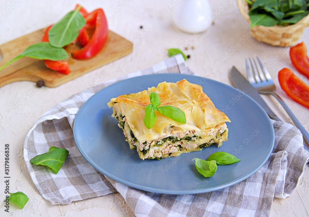Lasagna with salmon and spinach on a gray clay plate on a light concrete background. Italian food. Pasta Recipes Lasagna with salmon and spinach on a gray clay plate on a light concrete background. Italian food. Pasta Recipes