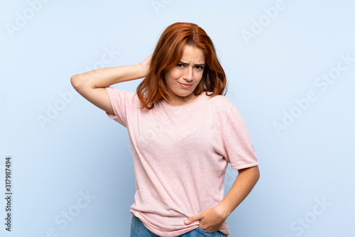 Teenager redhead girl over isolated blue background having doubts