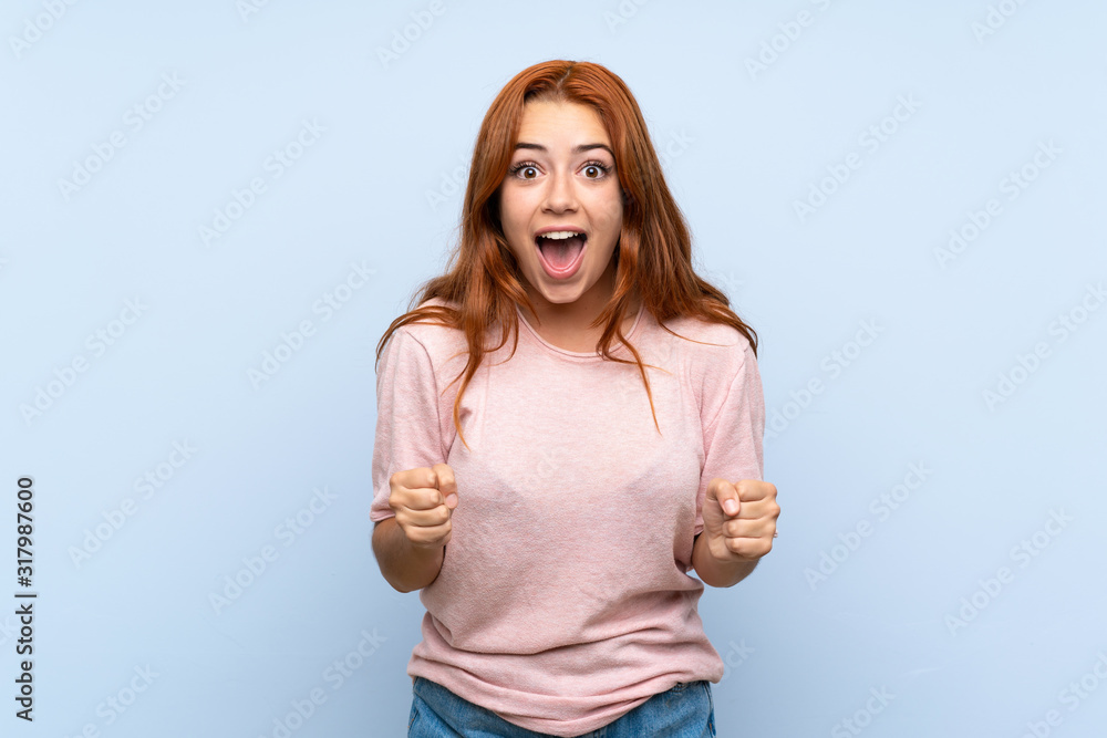 Fototapeta premium Teenager redhead girl over isolated blue background celebrating a victory in winner position