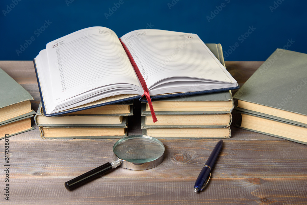 An open notebook, glasses, a pencil and books are on the table. An open notebook, glasses, a pencil and books are on the table.
