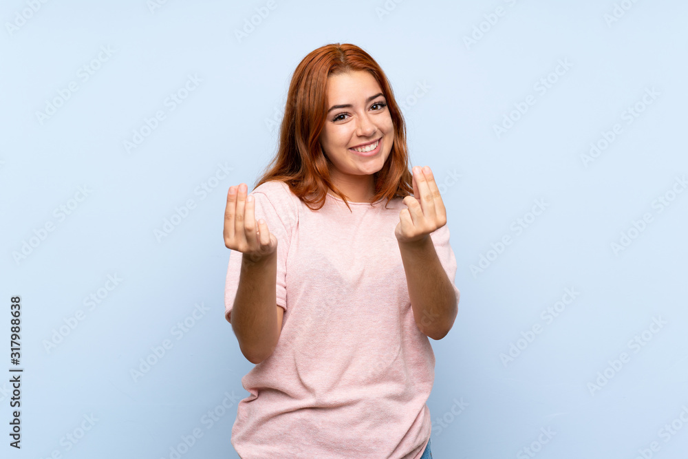 Teenager redhead girl over isolated blue background making money gesture Teenager redhead girl over isolated blue background making money gesture