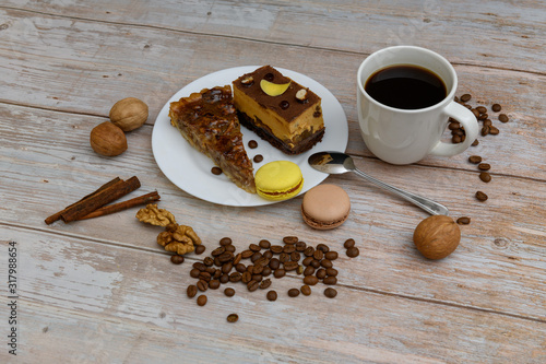 Cup of coffee and two slices of cake and macaroons on the plate on wooden table