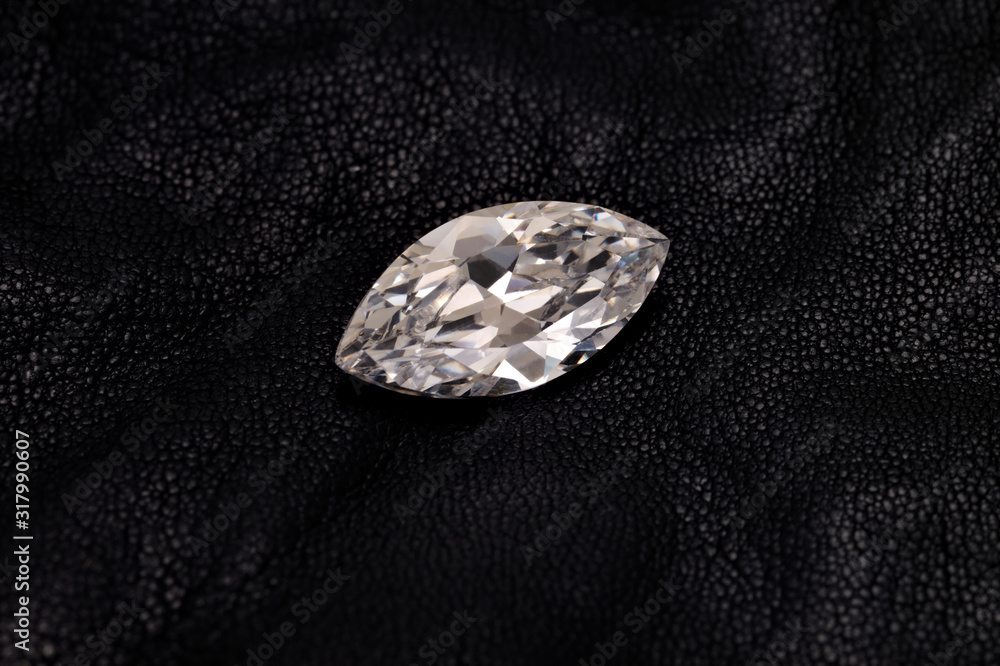 A faceted, round diamond sits isolated on a black leather background. A faceted, round diamond sits isolated on a black leather background.