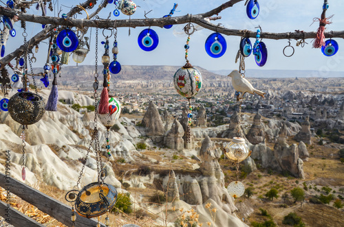 Evil Eye Beads on Tree and Fairy tale chimneys on background of blue sky in Pigeons Valley,Goreme,Turkey.Branches of the old tree decorated with the eye-shaped amulets Nazars Evil eye made of blue gla