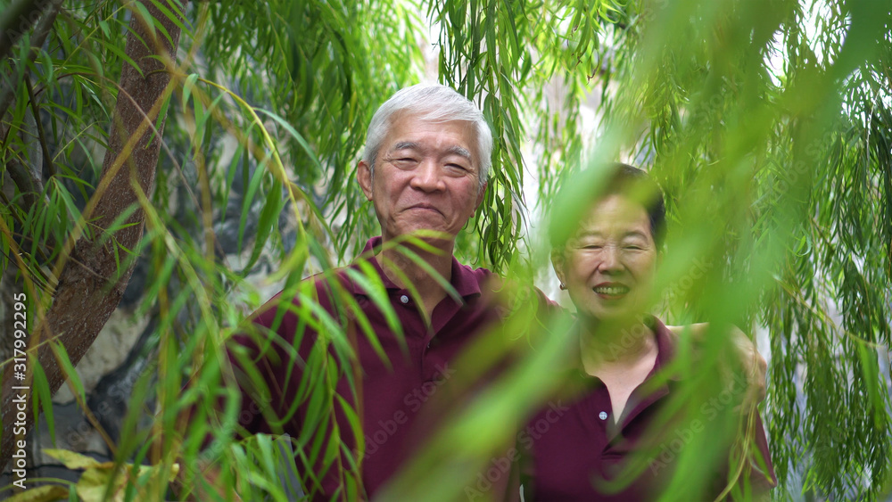 Happy retired Asian elder couple laughing under green willow tree Happy retired Asian elder couple laughing under green willow tree
