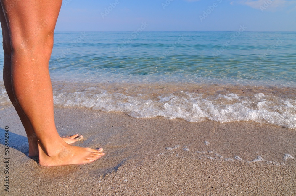 Beautiful female legs near sea waves on a sandy beach