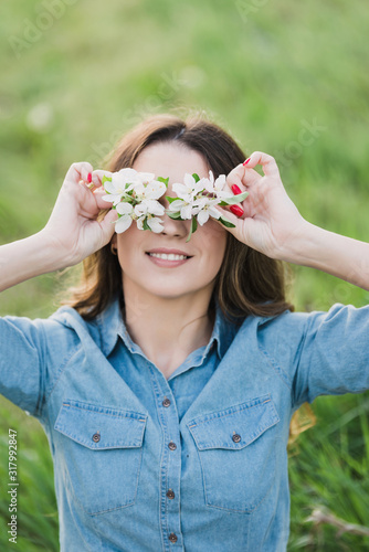 Pretty young woman hides her eyes behind flowers on fresh green grass background. Closeup portrait  in apricot blooming garden