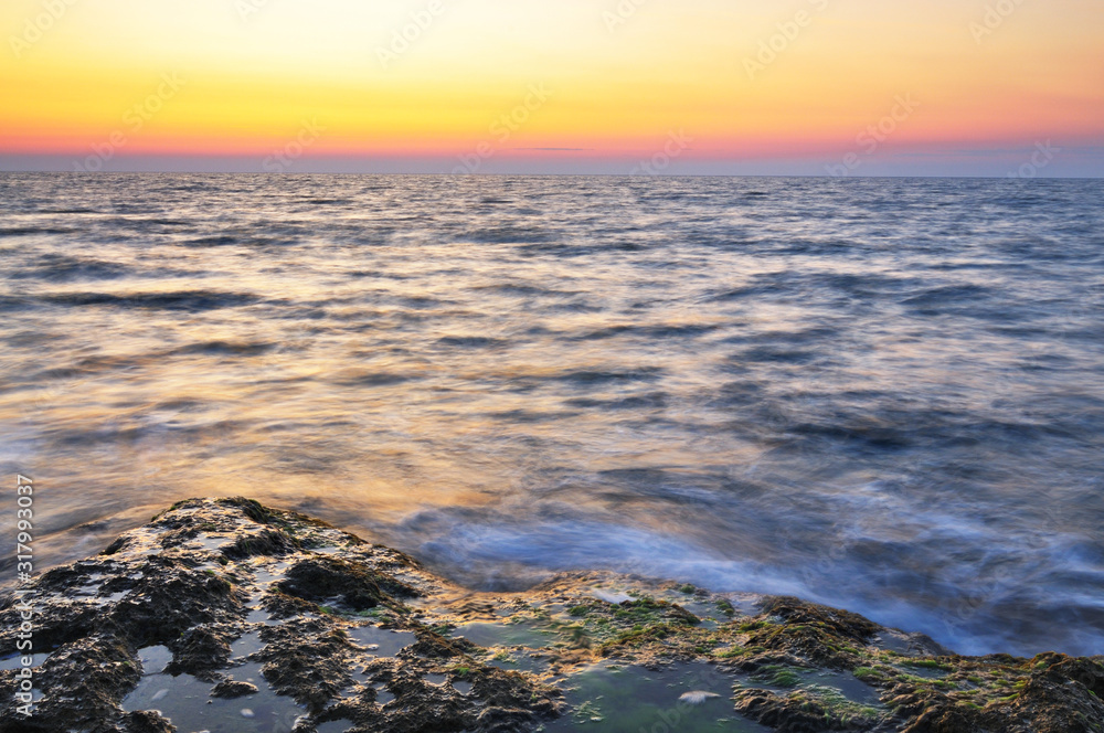Beautiful pink sunset and water stones with green moss over Black sea