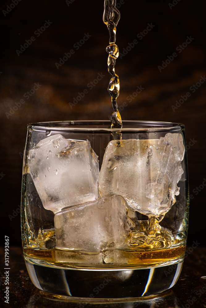 pour whiskey in a glass with ice on a dark wooden background close-up pour whiskey in a glass with ice on a dark wooden background close-up