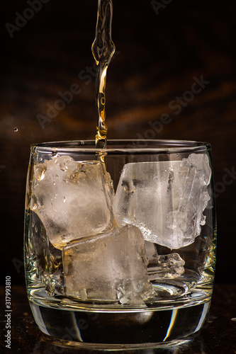 pour whiskey in a glass with ice on a dark wooden background close-up