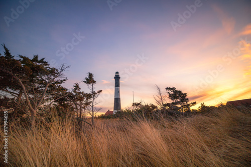 Golden sunset light illuminating beach grass in front of a stone lighthouse, with wispy clouds overhead in the sky. Fire Island National Seashore, New York. 