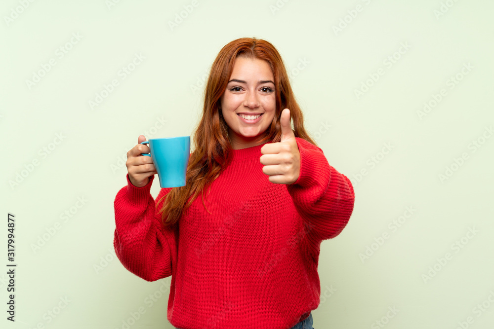 Teenager redhead girl with sweater over isolated green background holding hot cup of coffee Teenager redhead girl with sweater over isolated green background holding hot cup of coffee